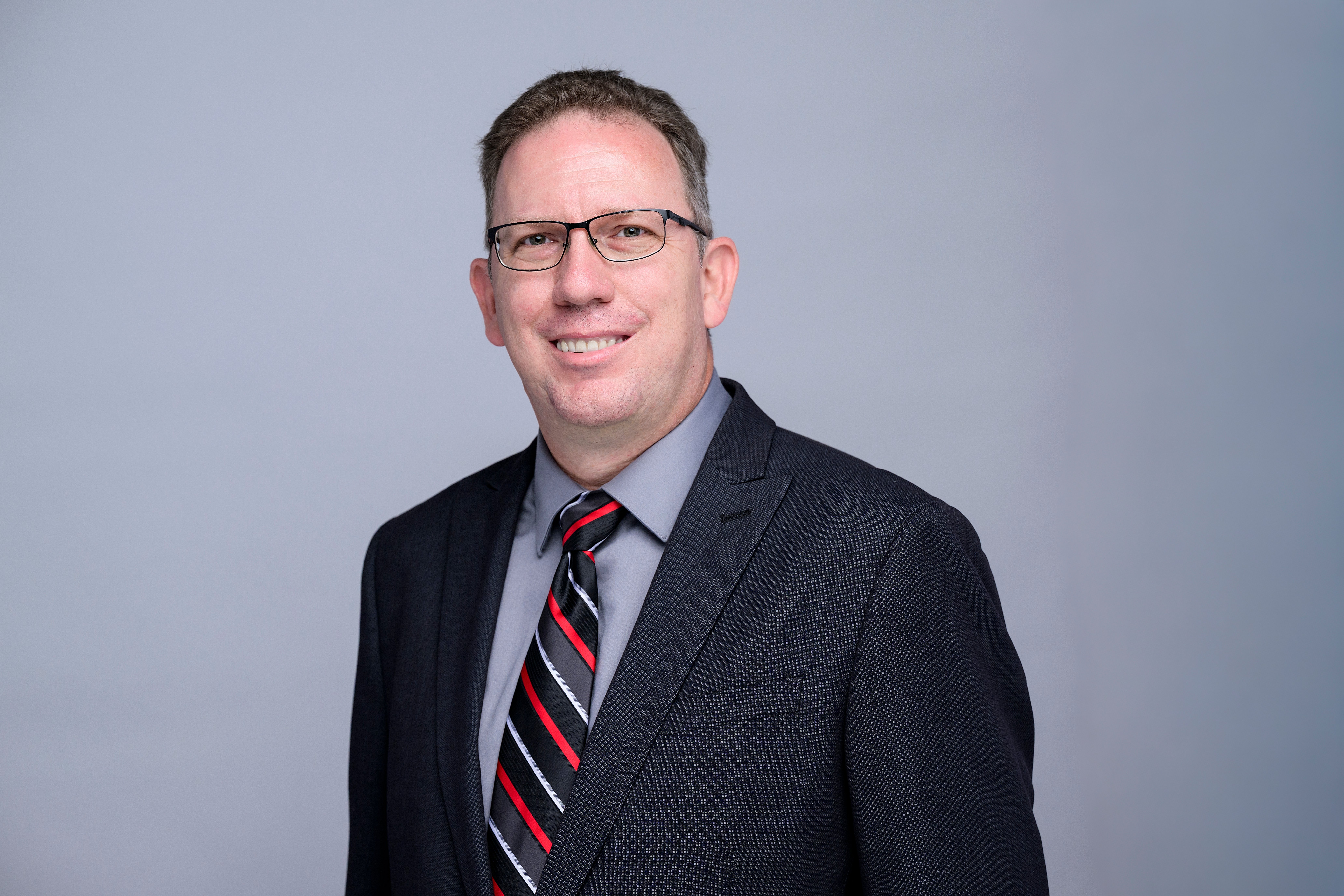 Kyle Headshot in black coat with grey shirt and background