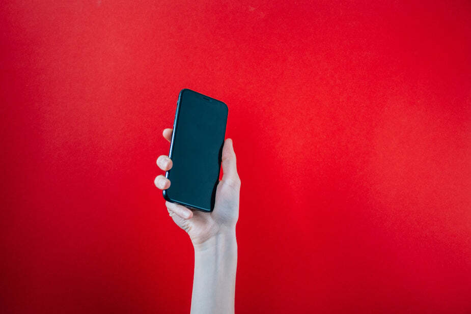 hand-holds-up-black-mobile-phone-on-red-background